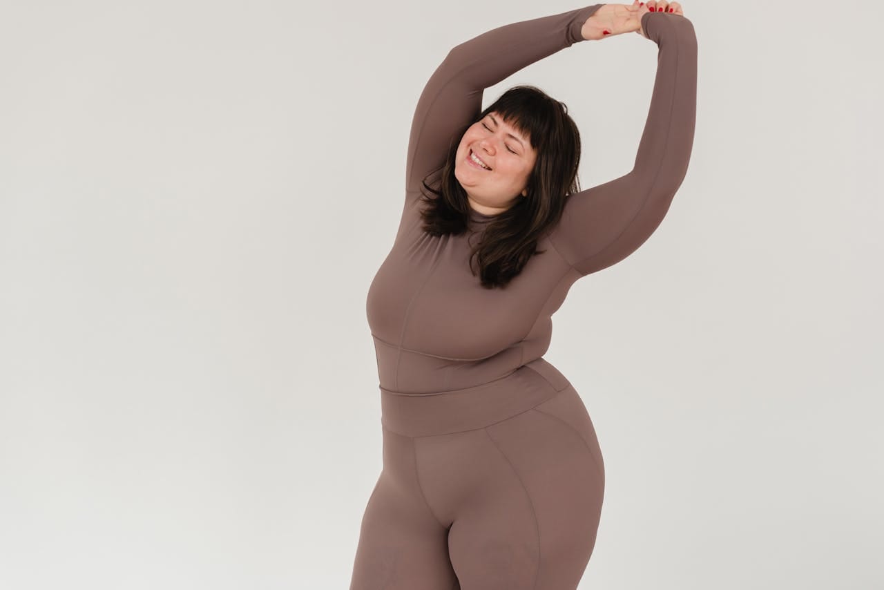 Happy plus-size woman in sportswear stretching confidently in a studio setting.