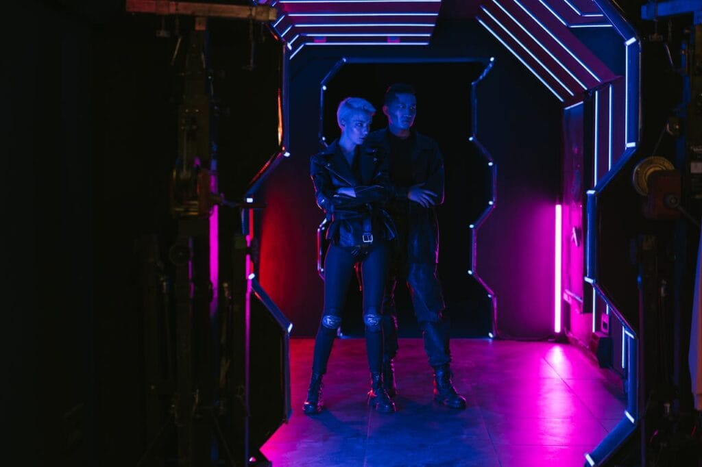Two adults in a neon-lit corridor displaying futuristic cyberpunk fashion style.